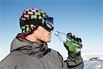 Young man in ski wear drinking water from a bottle, profile