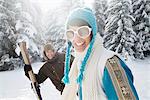 Junge Frau in Winterkleidung lächelnd in die Kamera, Mann, Ski im Hintergrund hält