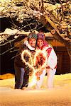 Young couple making heart shape with sparkler by night