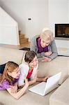 Two girls using a laptop on a couch with their grandmother standing beside them