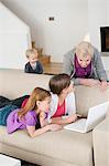 Two girls using a laptop on a couch with their grandmother