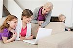 Two girls using a laptop on a couch with their grandmother standing beside them