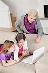 Deux jeunes filles, à l'aide d'un ordinateur portable sur un canapé avec leur grand-mère