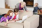 Zwei Mädchen mit einem Laptop auf der Couch mit ihrer Großmutter, die neben ihnen stehen