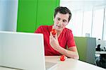 Businessman holding a tomato and using a laptop