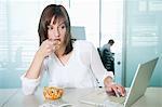 Femme d'affaires, manger des pâtes alimentaires et à l'aide d'un ordinateur portable