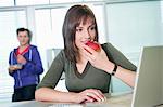 Businesswoman eating an apple and using a laptop