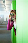 Businesswoman looking through binoculars in an office corridor