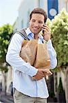 Mid homme adulte parlant sur un téléphone mobile avec les sacs en papier remplis de légumes