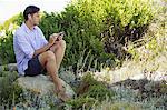 Mid adult man sitting on a rock and listening to music with an MP3 player