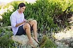 Mid adult man sitting on a rock and using a digital tablet