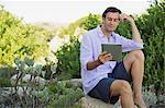 Mid adult man sitting on a rock and using a digital tablet