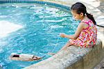 Fille assise au bord de la piscine en regardant bateau de jouet dans l'eau