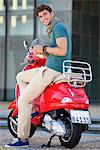 Portrait of young man sitting on a scooter and text messaging