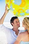 Homme soulevant un ballon de plage avec une femme près de lui