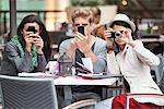 Three young friends using electronic gadgets in a restaurant