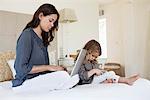 Woman working on a laptop with her daughter playing with a mobile phone beside her