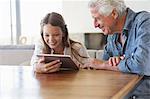 Mädchen mit einen digitalen Tablet mit ihrem Großvater sitzen in ihrer Nähe