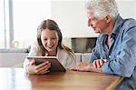 Girl using a digital tablet with her grandfather sitting near her