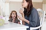 Young woman and little girl applying lip gloss at dressing table