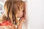 Cute little girl peeking into a dollhouse through the window