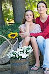 Petite fille et mère assise à l'extérieur avec des fleurs dans le panier