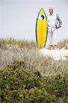 Senior man standing with surfboard on the beach