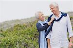 Senior woman putting sweater on husband's shoulder on the beach