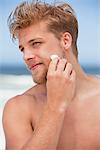 Young man applying moisturizer on his face