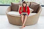 Fille assise dans un canapé en osier, en utilisant une tablette numérique