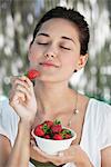 Beautiful young woman holding a bowl of strawberries with her eyes closed