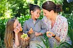 Happy mother eating fruits with her two daughters outdoors