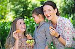 Happy mother eating fruits with her two daughters outdoors