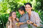 Happy mother eating fruits with her two daughters outdoors