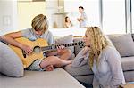 Teenage boy playing a guitar and his mother listening