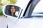 Reflet d'une jeune femme souriante sur un rétroviseur de voiture