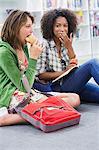 University student looking at her friend eating food in a library