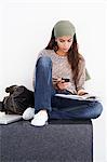 Beautiful woman using a mobile phone while reading book against white background