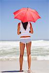 Femme debout sur la plage avec un parasol et de la recherche en mer vue