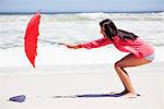 Femme en train de tenir un parapluie dans le vent fort sur la plage