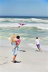 Mother carrying child while man flying kite on the beach