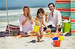 Mädchen spielen mit ihren Eltern hinter ihr sitzt am Strand