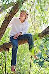 Happy little boy sitting on tree branch