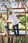 Rear view of children climbing ladders to tree house