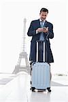 Homme debout avec des bagages à l'aide d'un téléphone mobile avec la tour Eiffel en arrière-plan, Paris, Ile-de-France, France