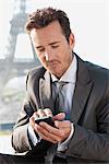 Homme d'affaires à l'aide d'un téléphone mobile avec la tour Eiffel en arrière-plan, Paris, Ile-de-France, France