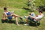 Man using a laptop with a woman reading a magazine in garden, Jardin des Tuileries, Paris, Ile-de-France, France