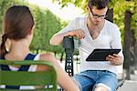 Aide d'une tablette numérique avec une femme assise en face de lui, Jardin des Tuileries, Paris, Ile-de-France, France