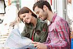 Couple sitting at a sidewalk cafe and reading a map, Paris, Ile-de-France, France