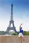 Woman holding a replica of Eiffel Tower sitting on a stone wall with the Eiffel Tower in the background, Paris, Ile-de-France, France